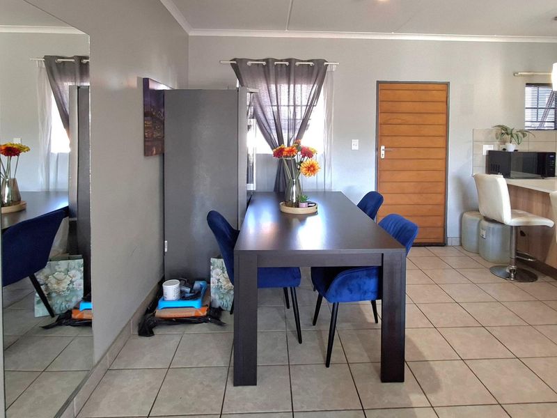 Open plan dining and kitchen area featuring tiled flooring, a breakfast bar, and a large wall mirror, creating a functional living space.