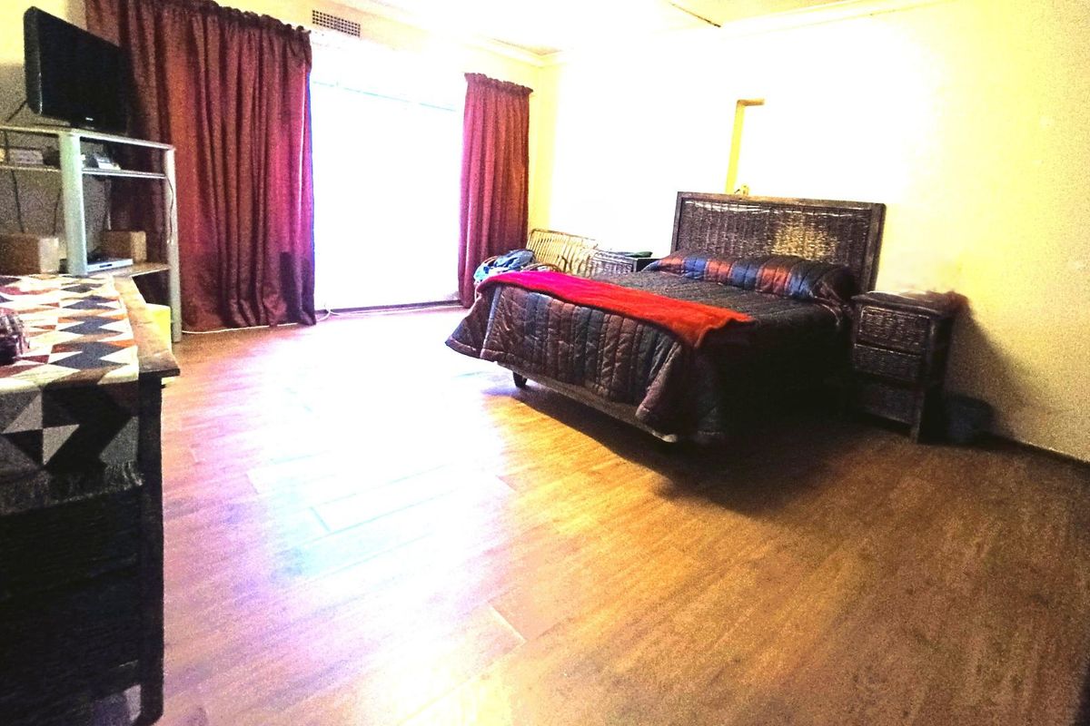 Spacious bedroom featuring wood-look flooring, large window with curtains, and neutral wall finishes.