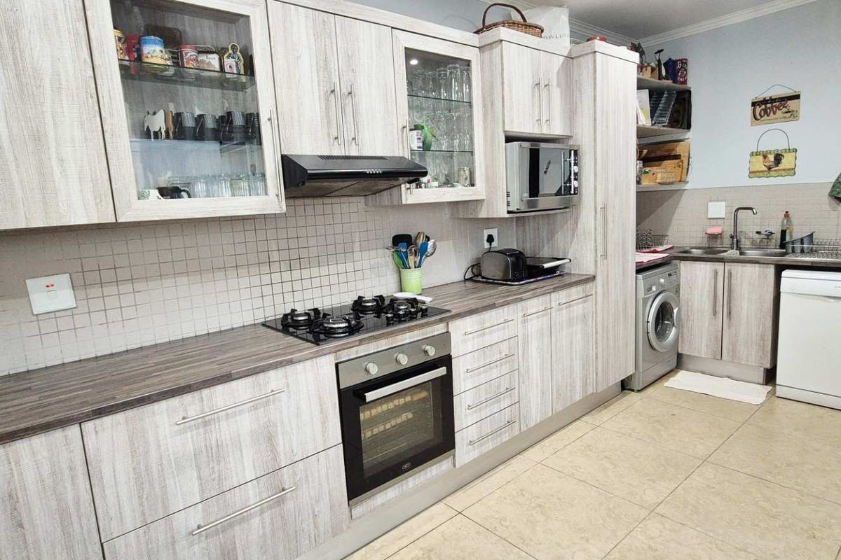 A functional kitchen featuring light wood-grain cabinetry, a built-in oven, gas hob, extractor fan, and integrated space for laundry and dishwashing appliances.