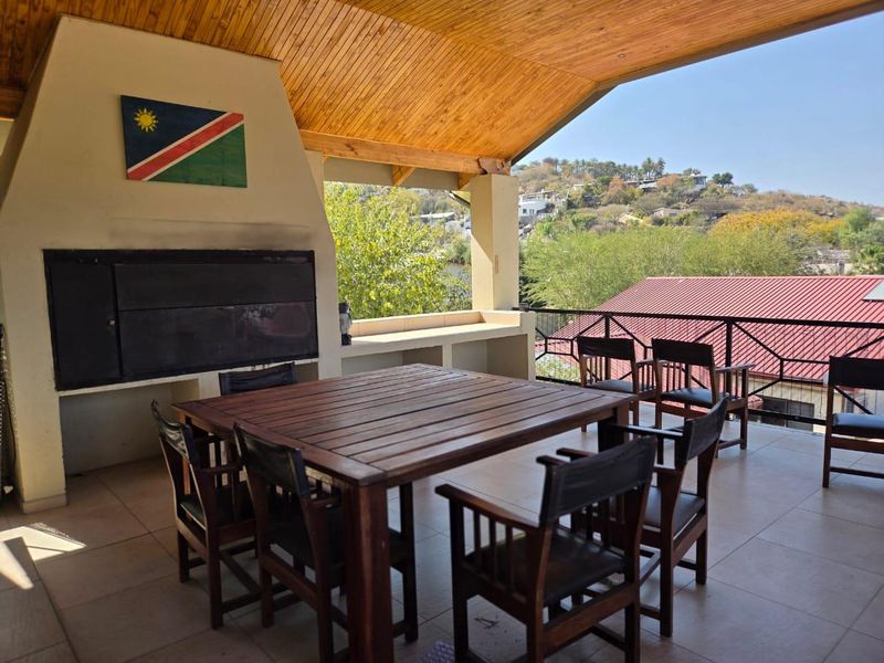 Covered outdoor patio featuring a built-in braai, concrete prep counter, timber ceiling, and metal balustrade with scenic elevated views.