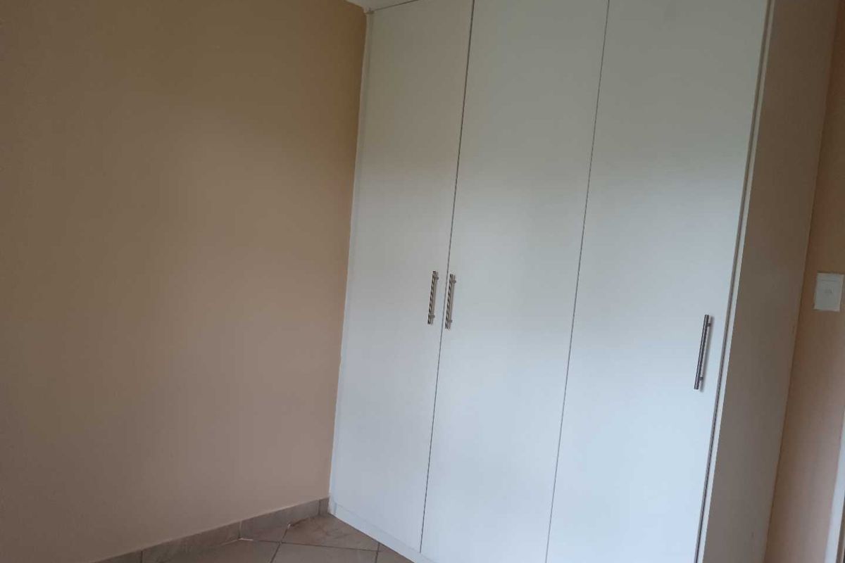 A bedroom featuring built-in white cabinetry with modern handles and tiled flooring.