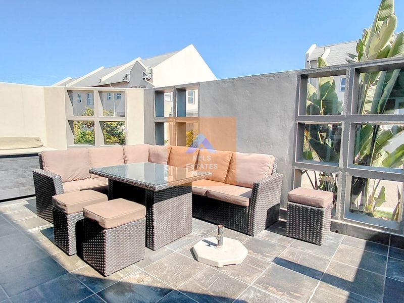An outdoor patio area featuring tiled flooring and a concrete privacy wall with decorative screen blocks, suitable for alfresco dining and relaxation.