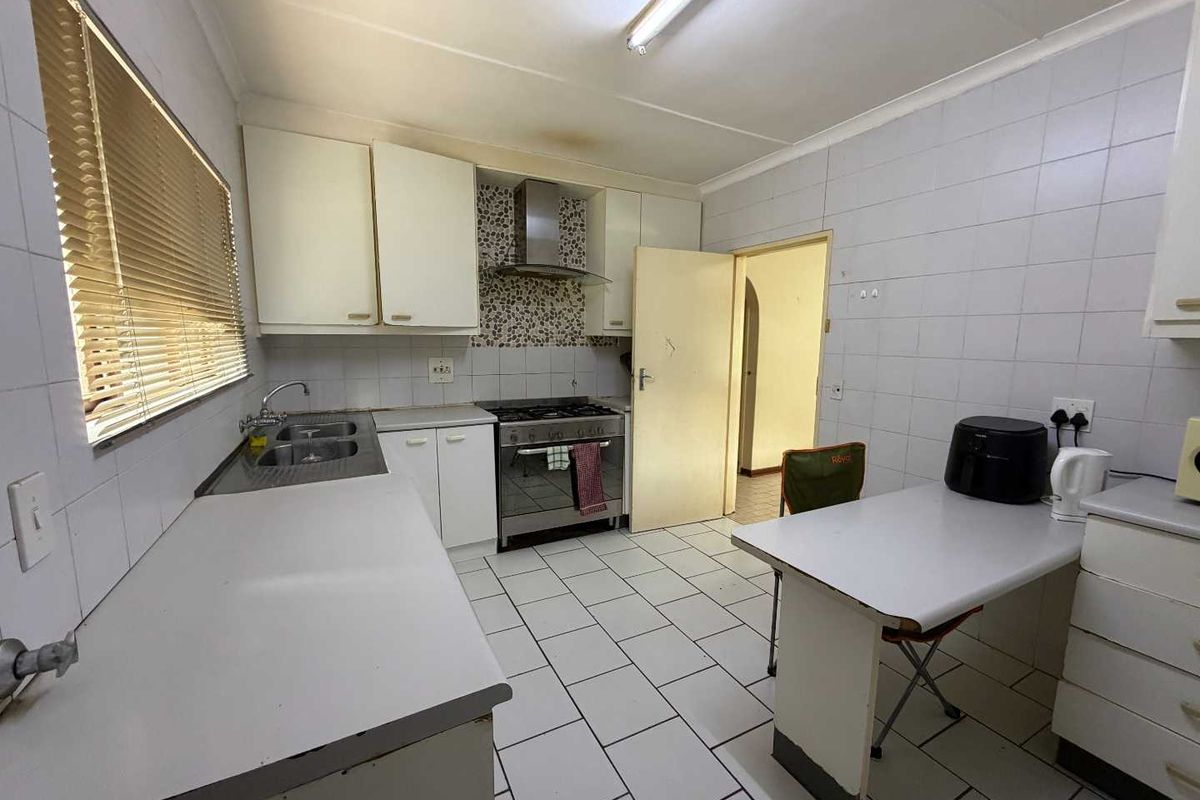 A functional kitchen featuring white cabinetry, tiled walls, a stainless steel sink, and a built-in stove with an extractor fan.