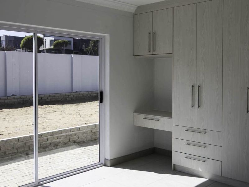 A bright, modern bedroom featuring neutral built-in cabinetry, a integrated desk, and large sliding glass doors opening to an outdoor area.