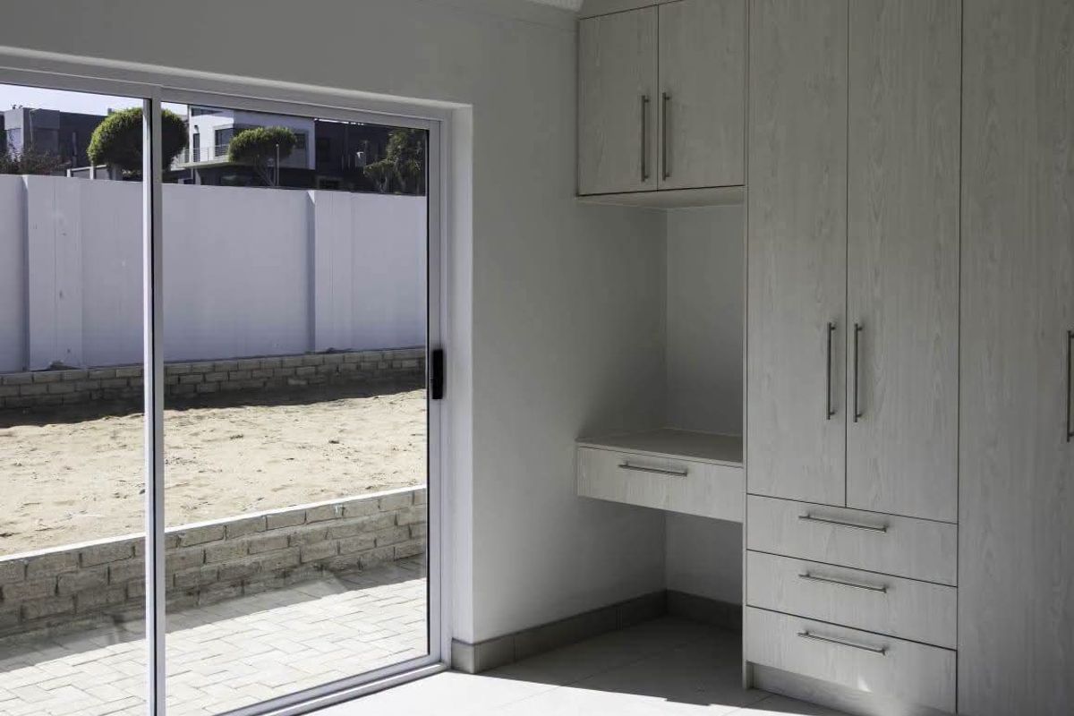 A bright, modern bedroom featuring neutral built-in cabinetry, a integrated desk, and large sliding glass doors opening to an outdoor area.
