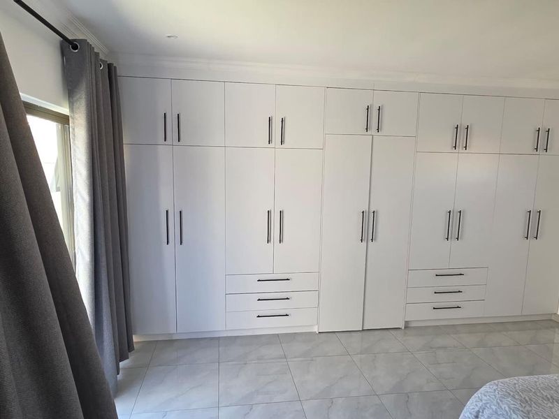 A well-maintained bedroom featuring extensive floor-to-ceiling built-in cupboards, modern tiled flooring, and clean finishes throughout.
