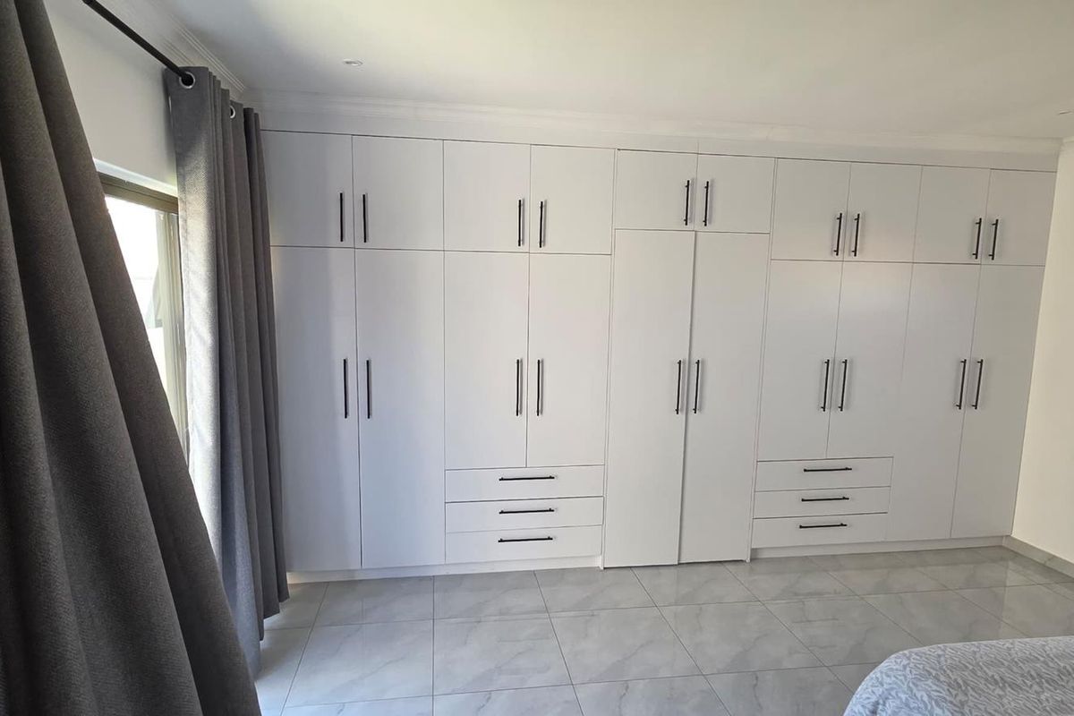 A well-maintained bedroom featuring extensive floor-to-ceiling built-in cupboards, modern tiled flooring, and clean finishes throughout.