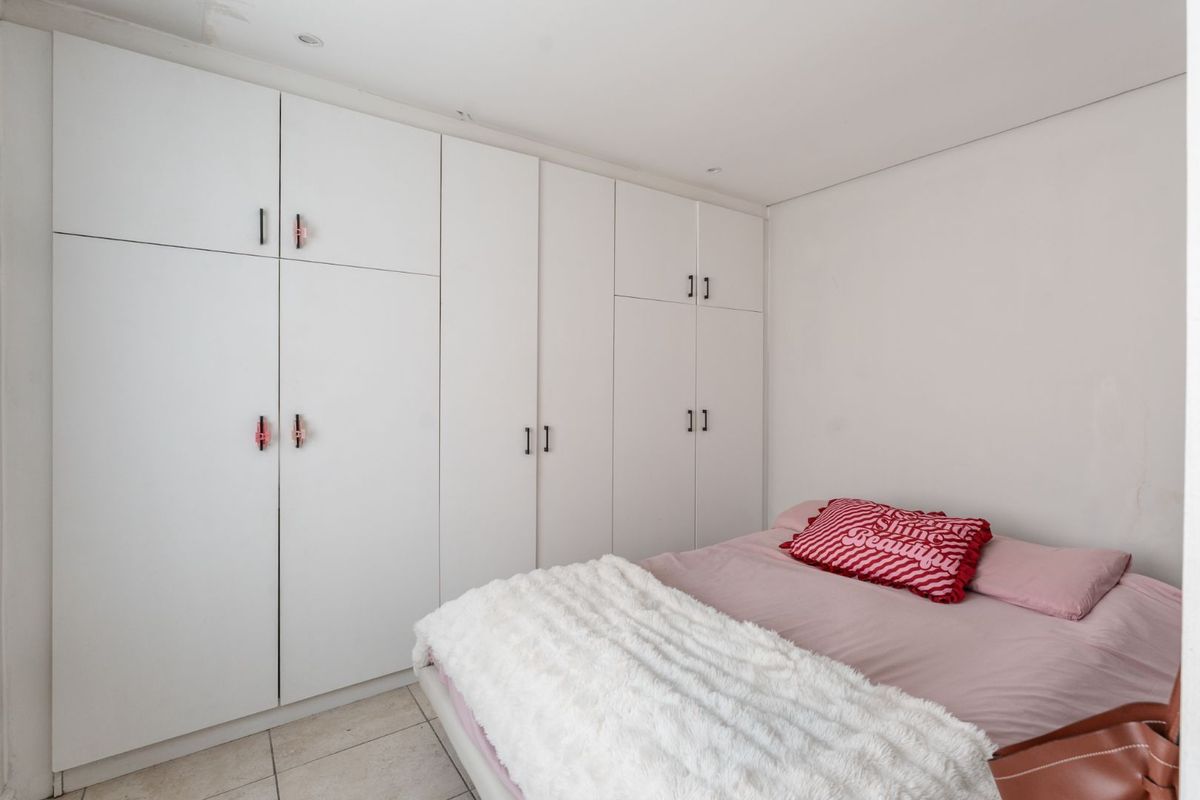 A clean bedroom featuring extensive white built-in cupboards providing ample storage, complemented by neutral tiled flooring and recessed ceiling lighting.