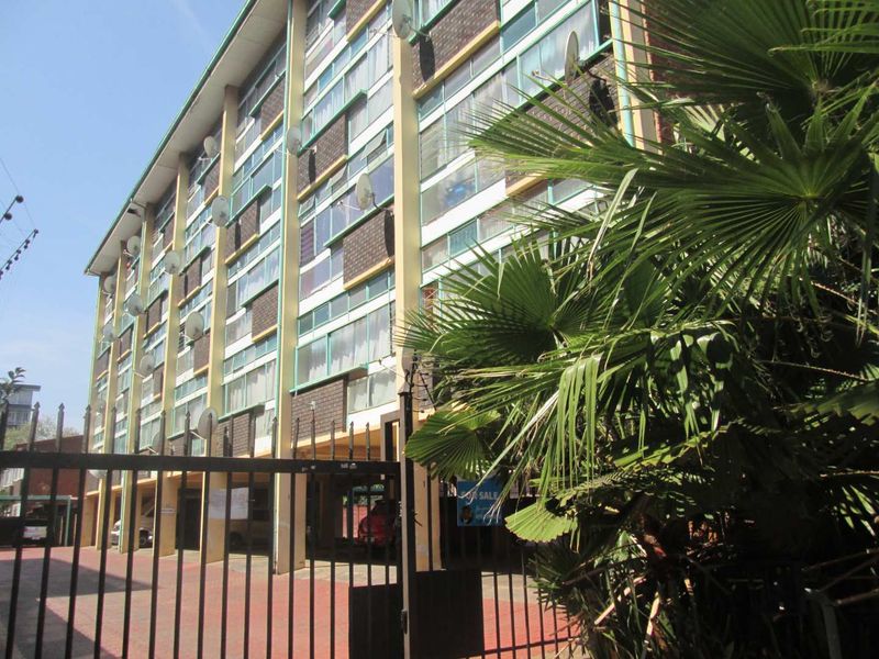 Exterior view of a multi-story apartment building featuring a brick facade, large windows, and a secure gated entrance.
