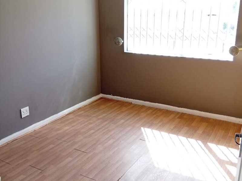 An empty bedroom featuring laminate flooring with visible wear and security bars on the window.