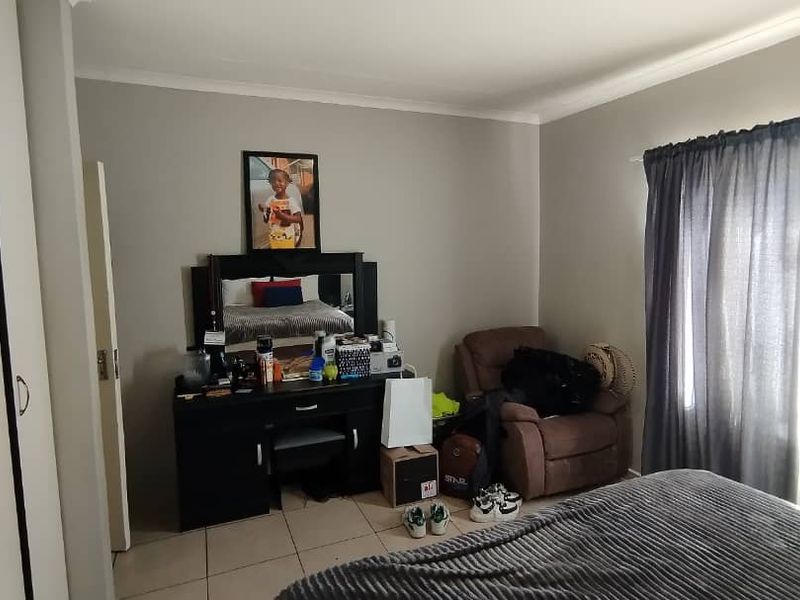 A functional bedroom featuring built-in cupboards, tiled flooring, and natural light through window curtains.