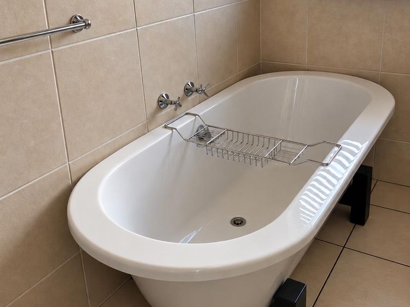 A well-maintained bathroom featuring a modern freestanding bathtub, neutral ceramic tiling, and a window with a venetian blind.