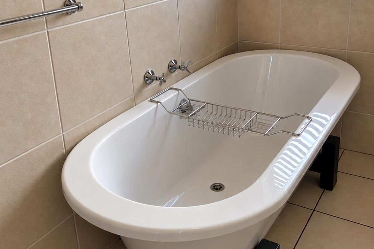 A well-maintained bathroom featuring a modern freestanding bathtub, neutral ceramic tiling, and a window with a venetian blind.