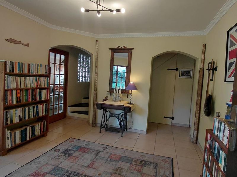 A living area featuring tiled flooring, crown molding, and an arched entryway leading to a staircase with glass block detailing.