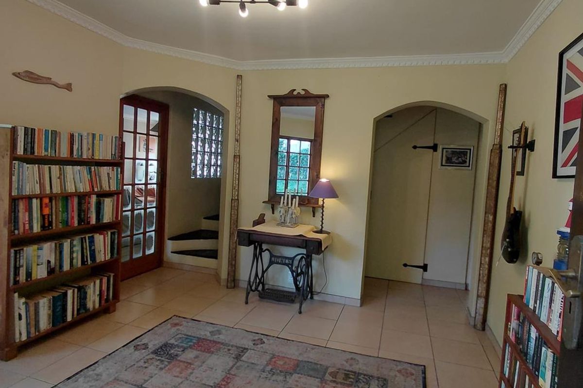 A living area featuring tiled flooring, crown molding, and an arched entryway leading to a staircase with glass block detailing.