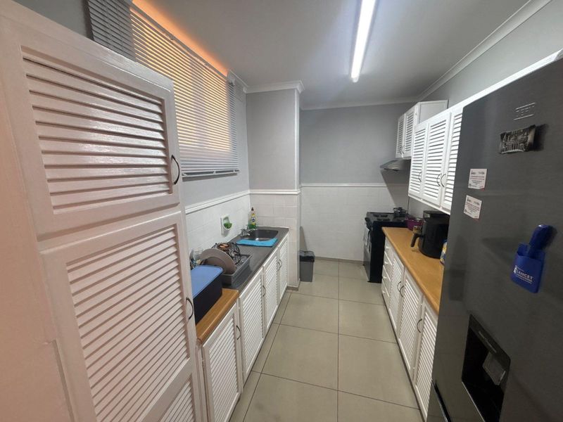 A functional galley-style kitchen featuring white louvered cabinetry, wooden countertops, tiled backsplash, and ceramic floor tiles.