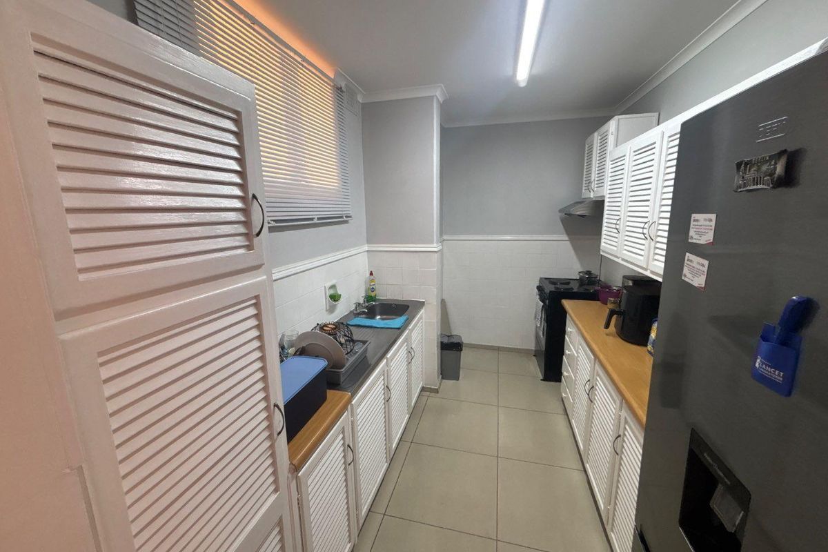 A functional galley-style kitchen featuring white louvered cabinetry, wooden countertops, tiled backsplash, and ceramic floor tiles.