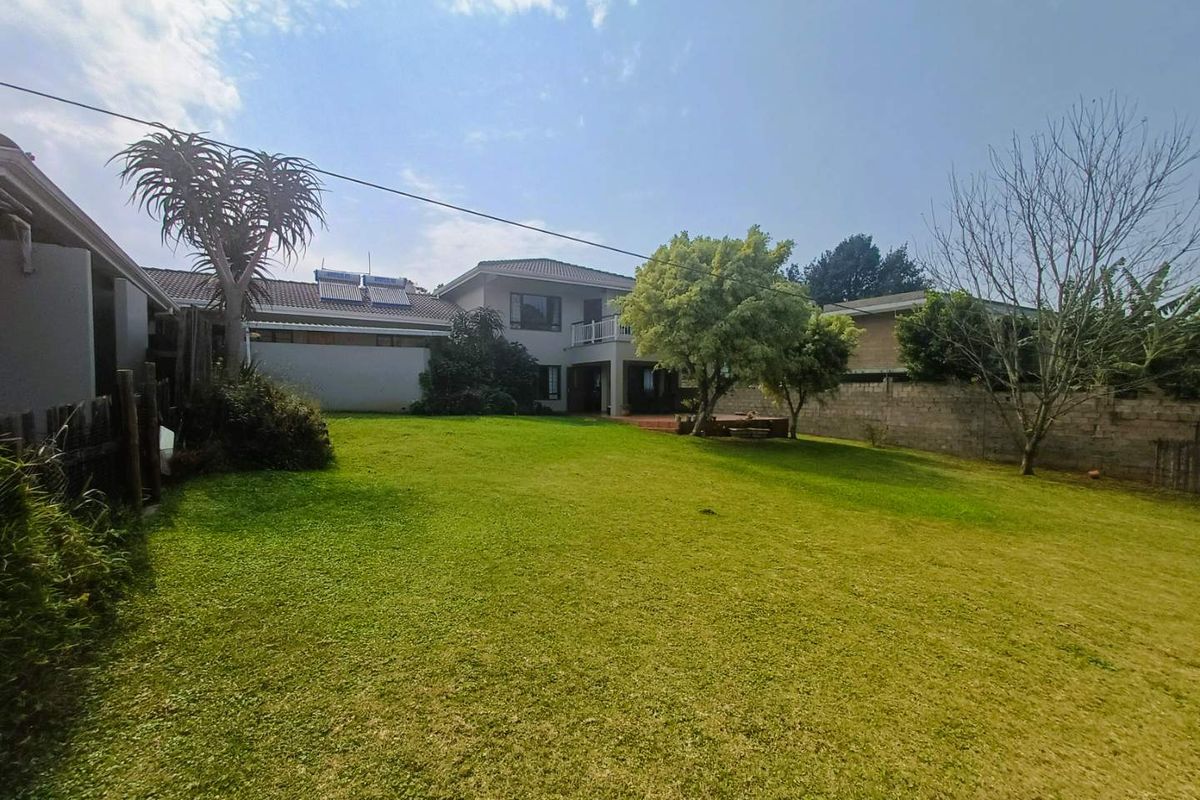 Spacious rear garden featuring a large lawn, mature trees, and a view of the two-story house exterior with a balcony and solar water heating system.