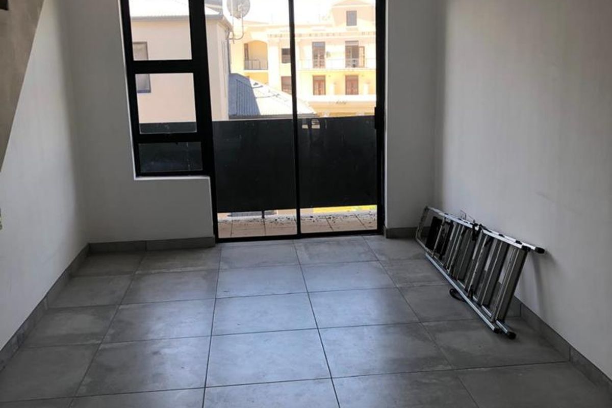 An empty living area featuring large format floor tiles, a staircase, and sliding glass doors leading to an outdoor balcony.