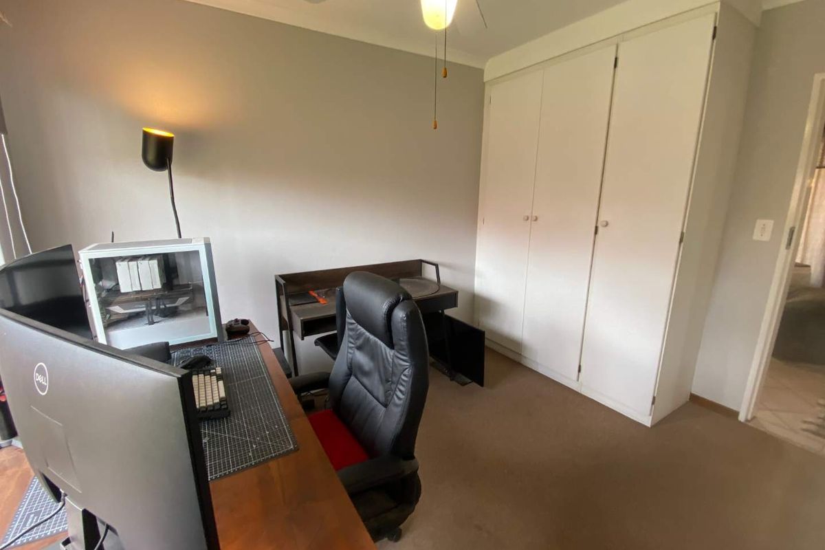 A bedroom featuring built-in cupboards, carpeted flooring, and a ceiling fan, currently utilized as a home office space.