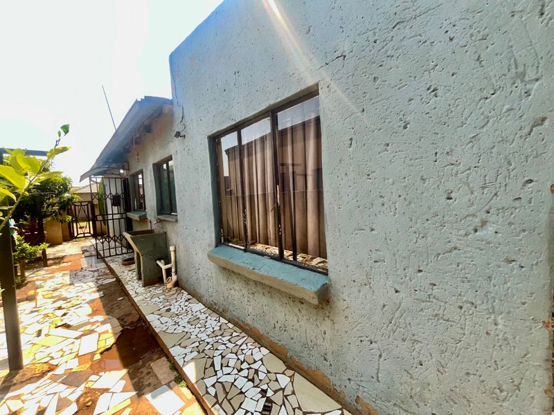 Rear exterior view of the property featuring a textured wall finish, aluminium windows, a concrete wash basin, and a tiled pathway.