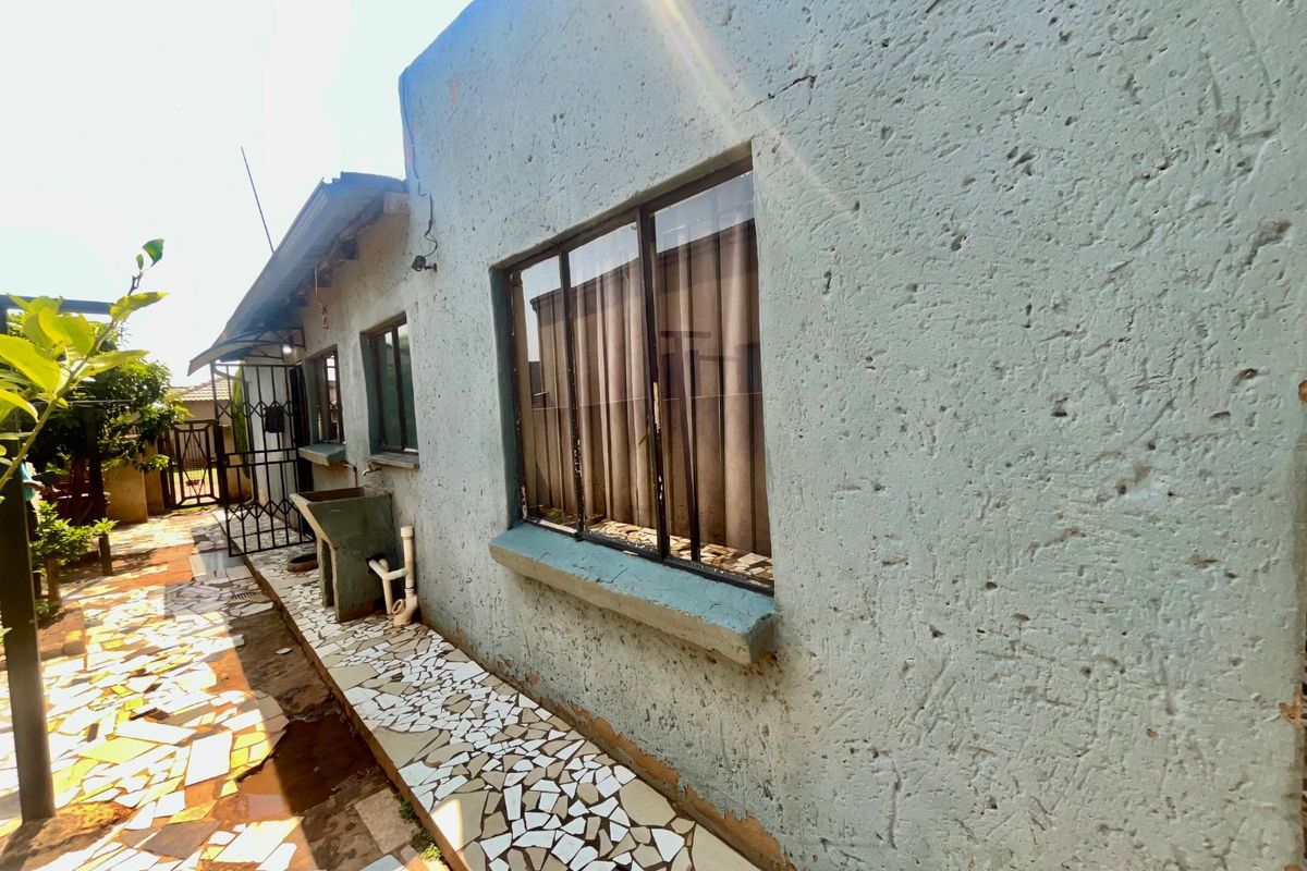 Rear exterior view of the property featuring a textured wall finish, aluminium windows, a concrete wash basin, and a tiled pathway.