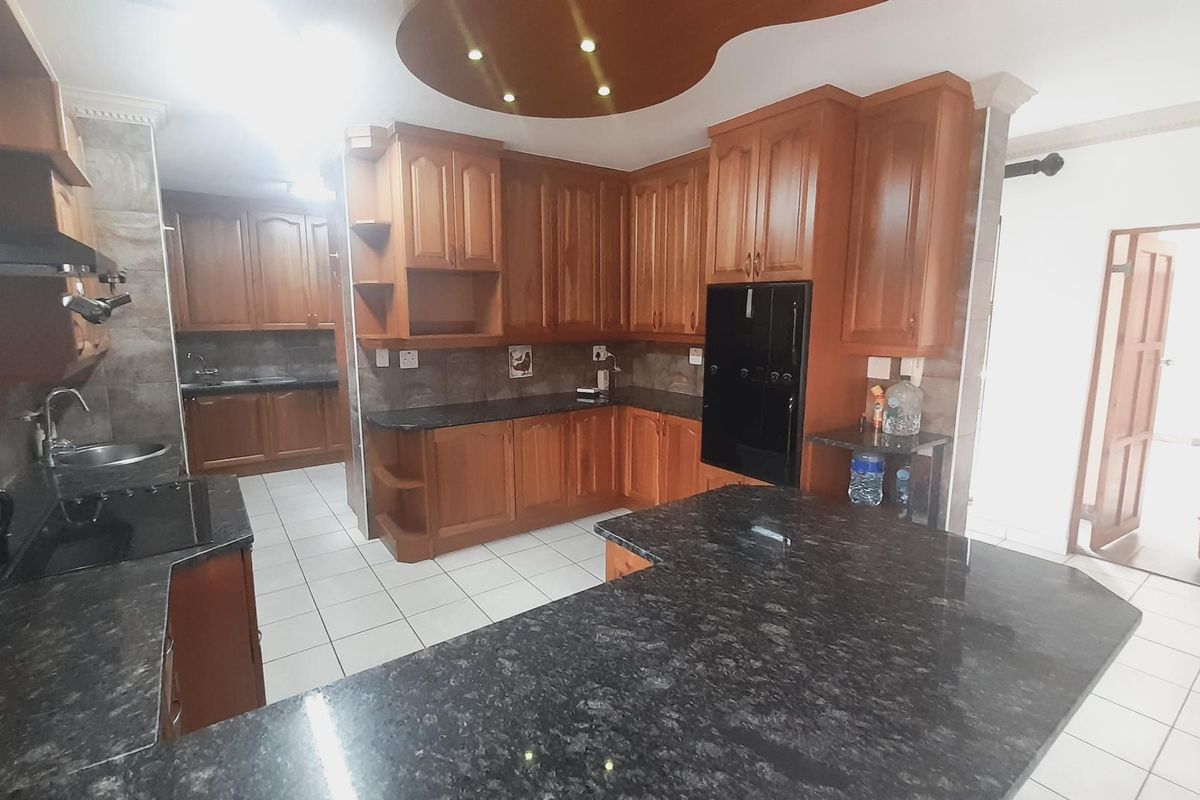 Spacious kitchen featuring dark granite countertops, extensive wooden cabinetry, tiled flooring, and a built-in oven, offering ample workspace and storage.