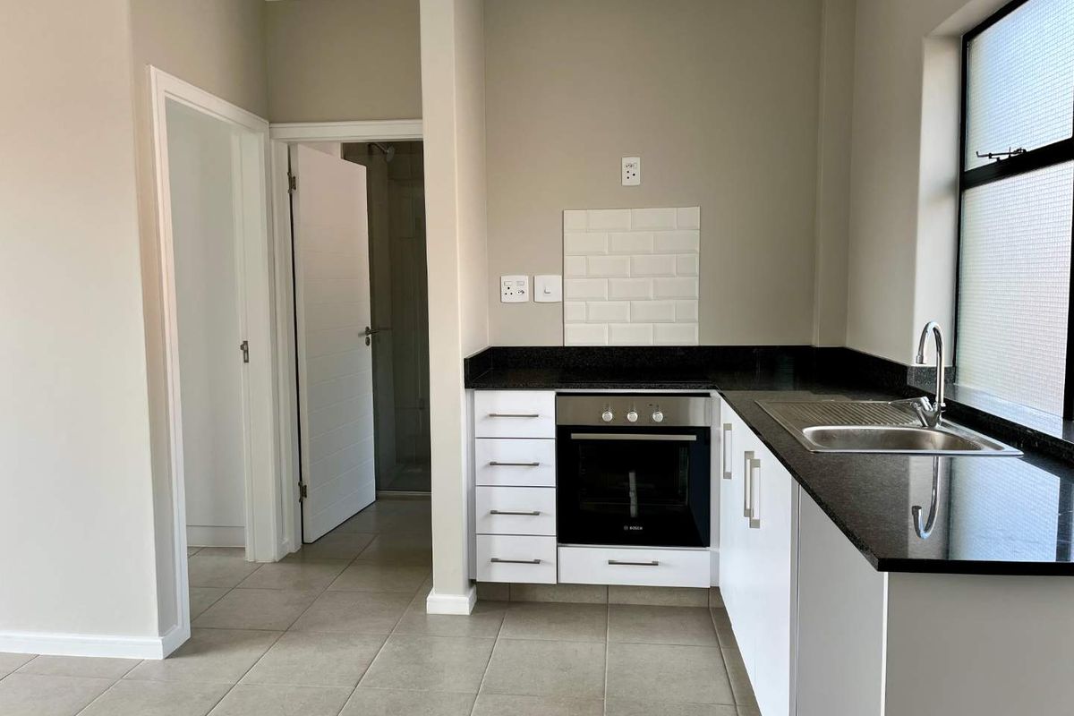 A clean, modern kitchen featuring granite countertops, built-in oven, subway tile backsplash, and neutral ceramic floor tiles.
