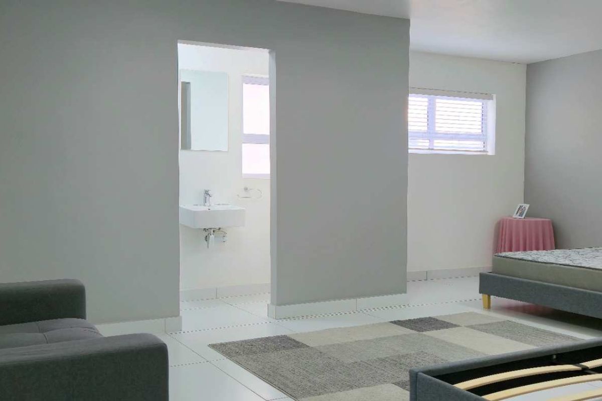 A spacious bedroom featuring neutral grey walls, tiled flooring, and an en-suite bathroom with a wall-mounted basin.