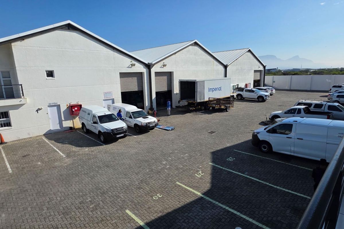 An elevated view of an industrial property courtyard featuring multiple roller shutter doors, paved parking bays, and access to warehouse units.