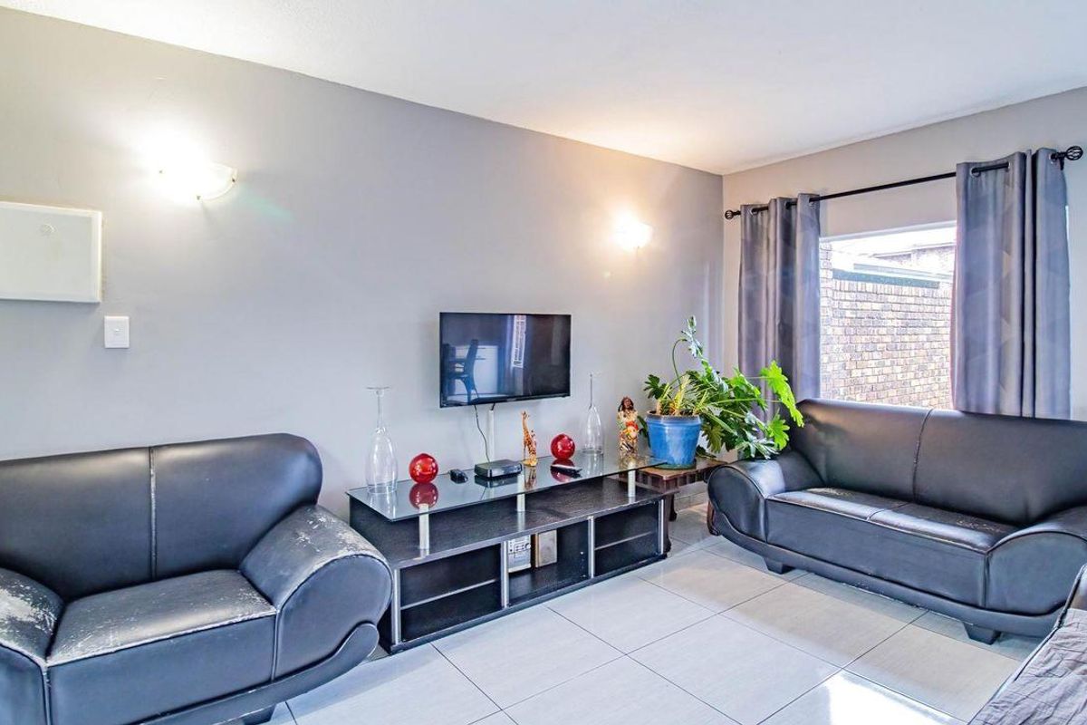 A comfortable living room featuring tiled flooring, wall-mounted lighting, and a window with curtain rails.