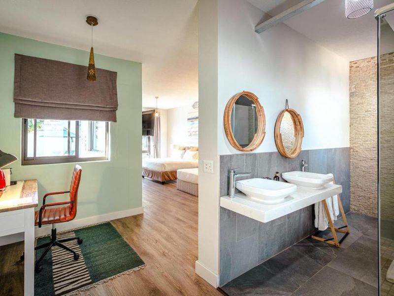 An open-plan guest suite featuring a modern bathroom with a double vanity, stone-tiled shower, and a connected bedroom area with wood-look flooring.