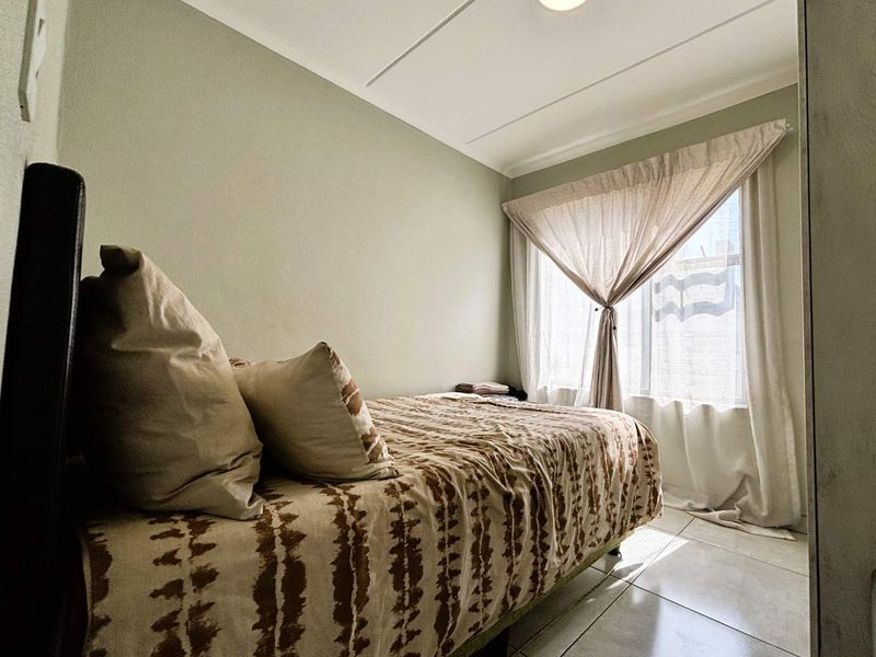 A compact bedroom featuring tiled flooring and natural light from a window with fitted curtains.