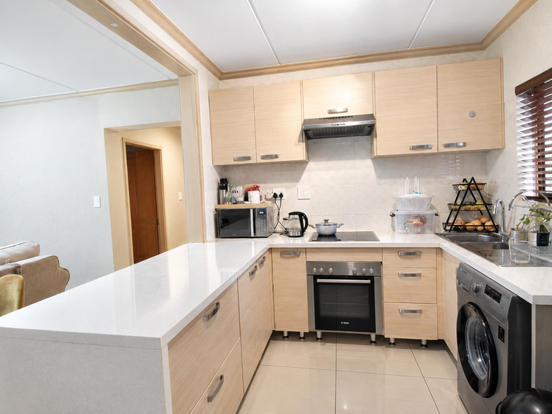 Modern kitchen featuring light wood cabinetry, stone countertops, integrated appliances, and tiled flooring, seamlessly flowing into the adjacent living area.