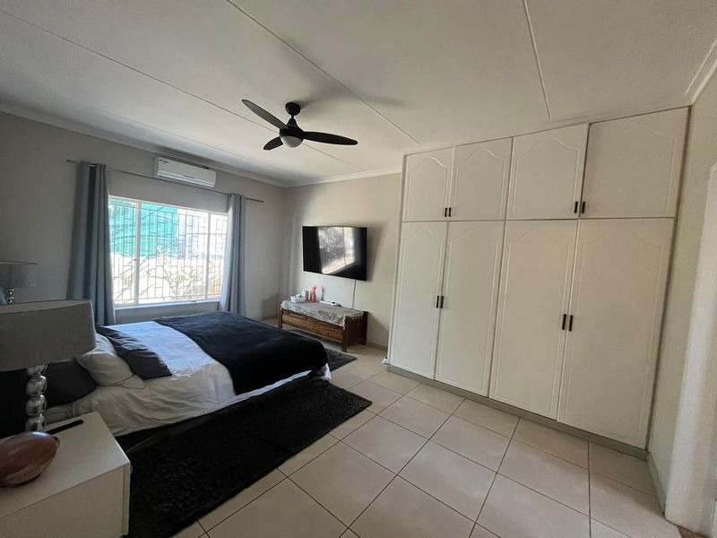 Spacious bedroom featuring tiled flooring, built-in cupboards, a ceiling fan, and an air conditioning unit for climate control.