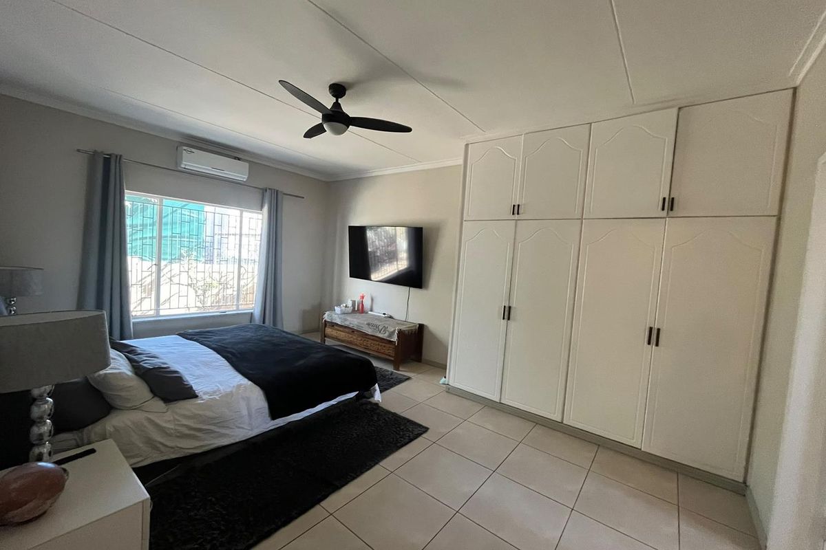 Spacious bedroom featuring tiled flooring, built-in cupboards, a ceiling fan, and an air conditioning unit for climate control.