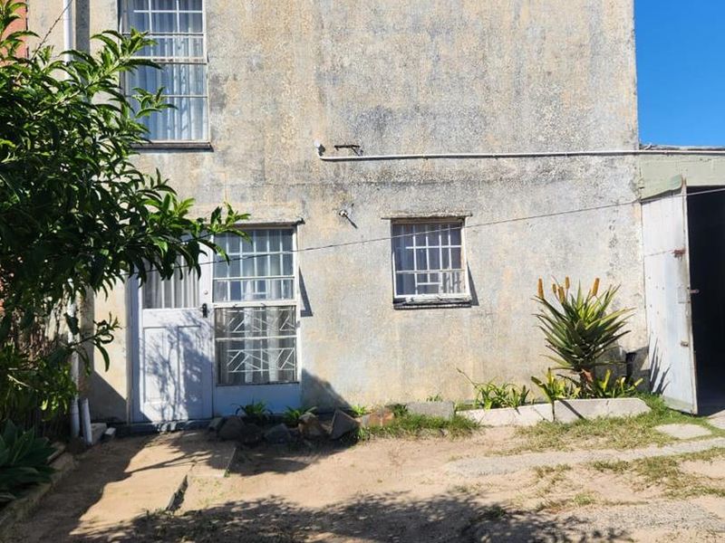 Rear exterior view of the property showing a weathered facade, security bars on windows, and an unpaved yard area.