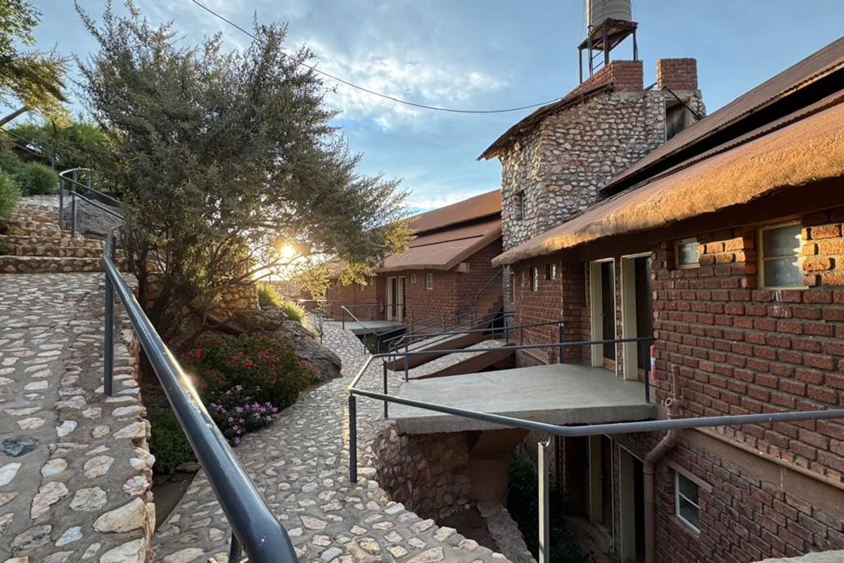 Exterior view of a lodge featuring rustic brick architecture, stone pathways, and elevated walkways set within a natural landscape.