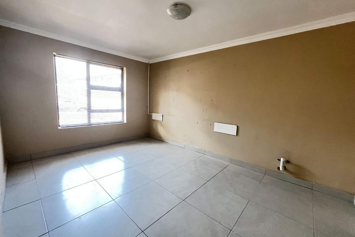 An empty bedroom featuring tiled flooring, a large window, and neutral wall finishes, requiring minor cosmetic repairs to the walls and plumbing area.