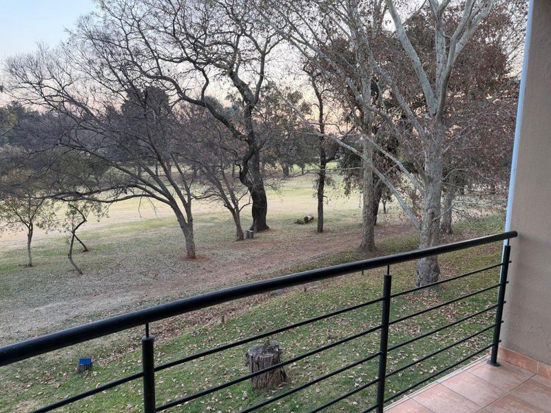 A balcony featuring a metal balustrade and tiled flooring, offering an open view of the surrounding parkland and trees.