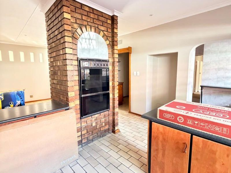 A spacious kitchen area featuring a distinctive brick pillar with a built-in double oven, tiled flooring, and an open-plan layout.