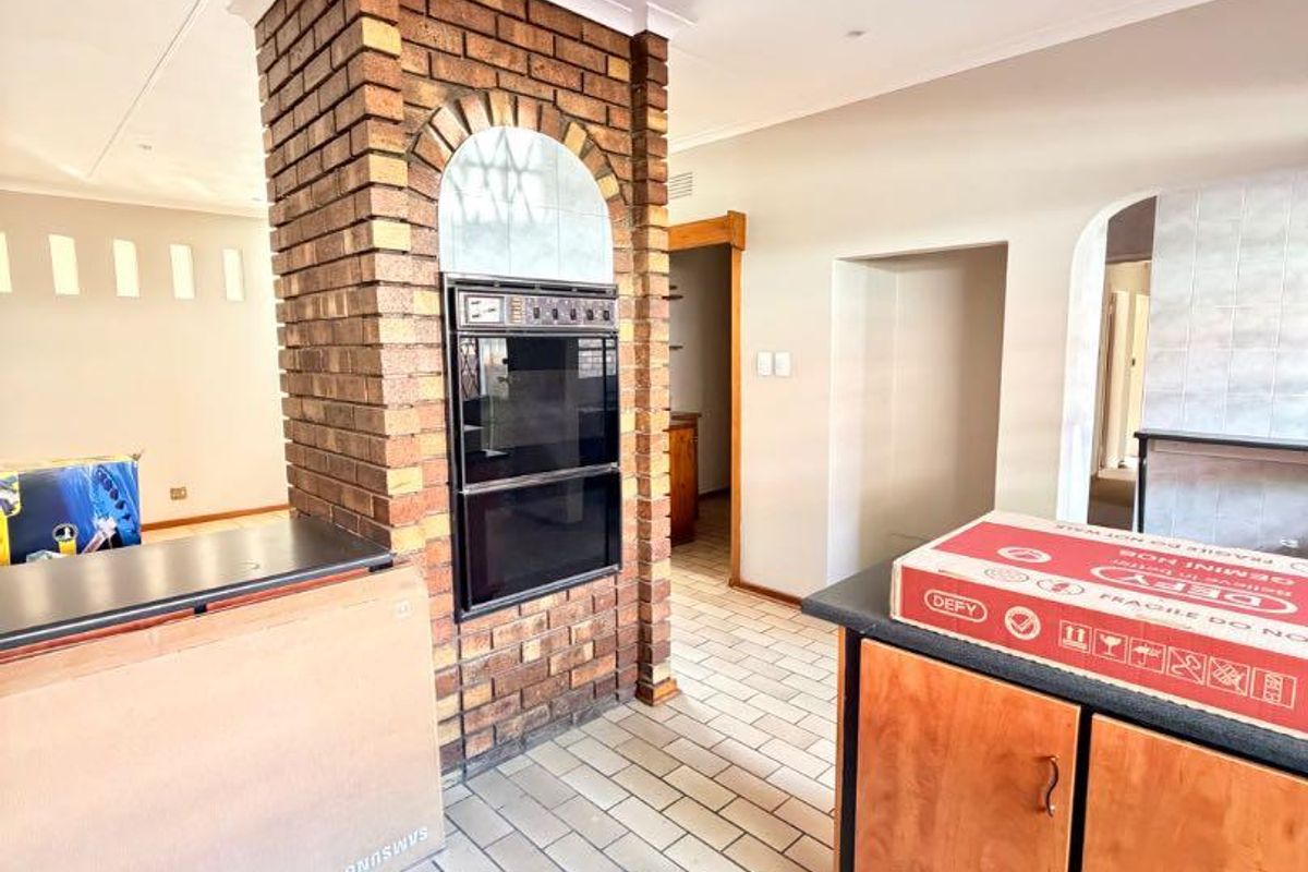 A spacious kitchen area featuring a distinctive brick pillar with a built-in double oven, tiled flooring, and an open-plan layout.