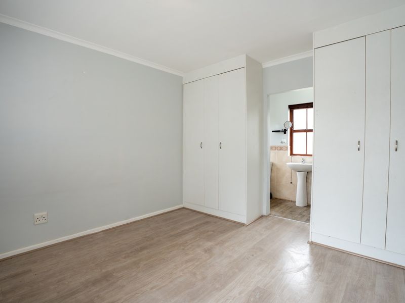 A bright, empty bedroom featuring neutral walls, laminate flooring, and built-in cupboards, with an adjoining en-suite bathroom area.