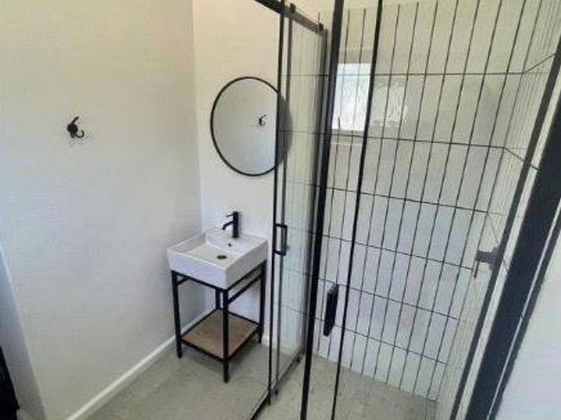 Modern bathroom featuring a glass-enclosed shower with black frame, rain shower head, and a contemporary vessel sink with wall-mounted faucet.