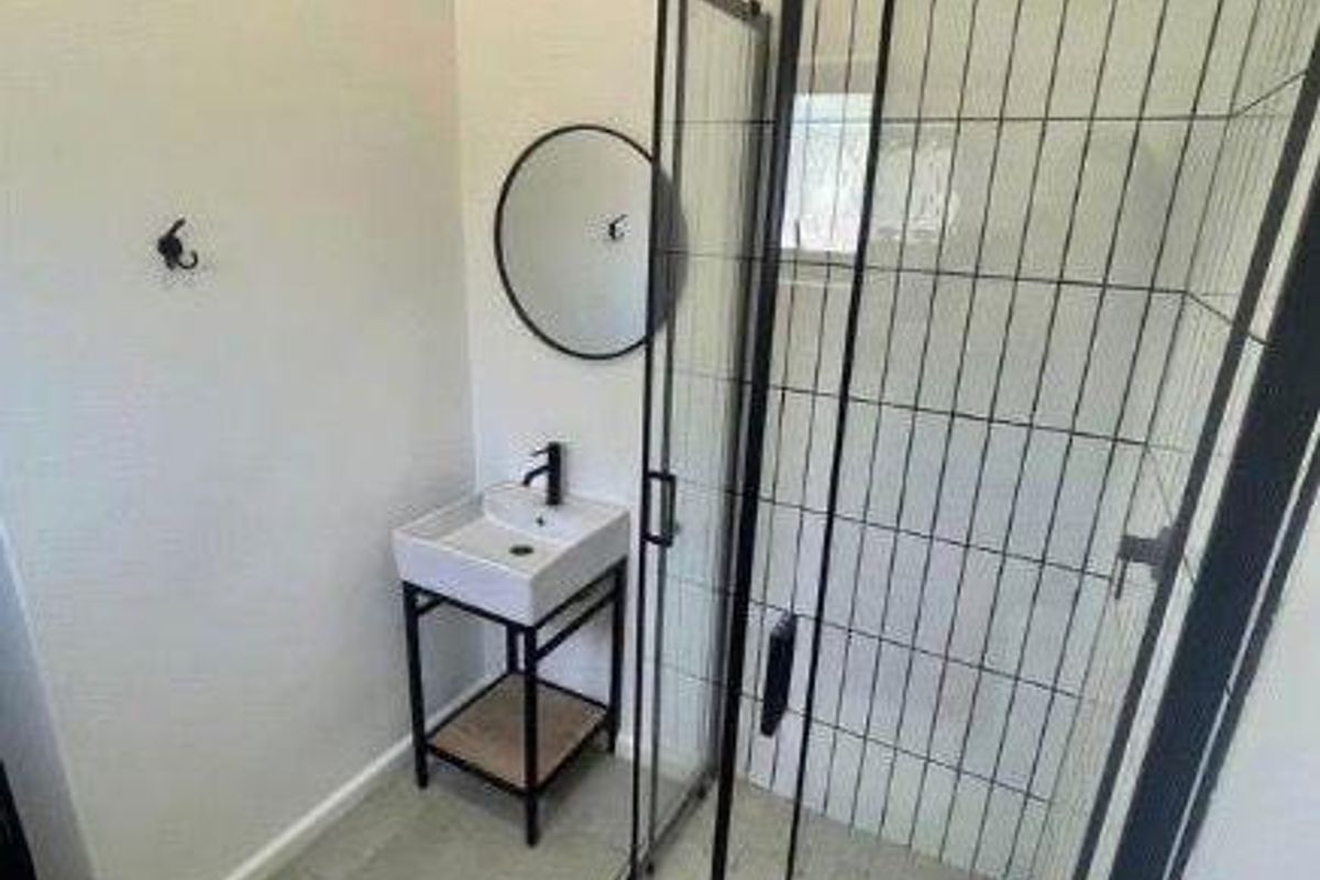Modern bathroom featuring a glass-enclosed shower with black frame, rain shower head, and a contemporary vessel sink with wall-mounted faucet.