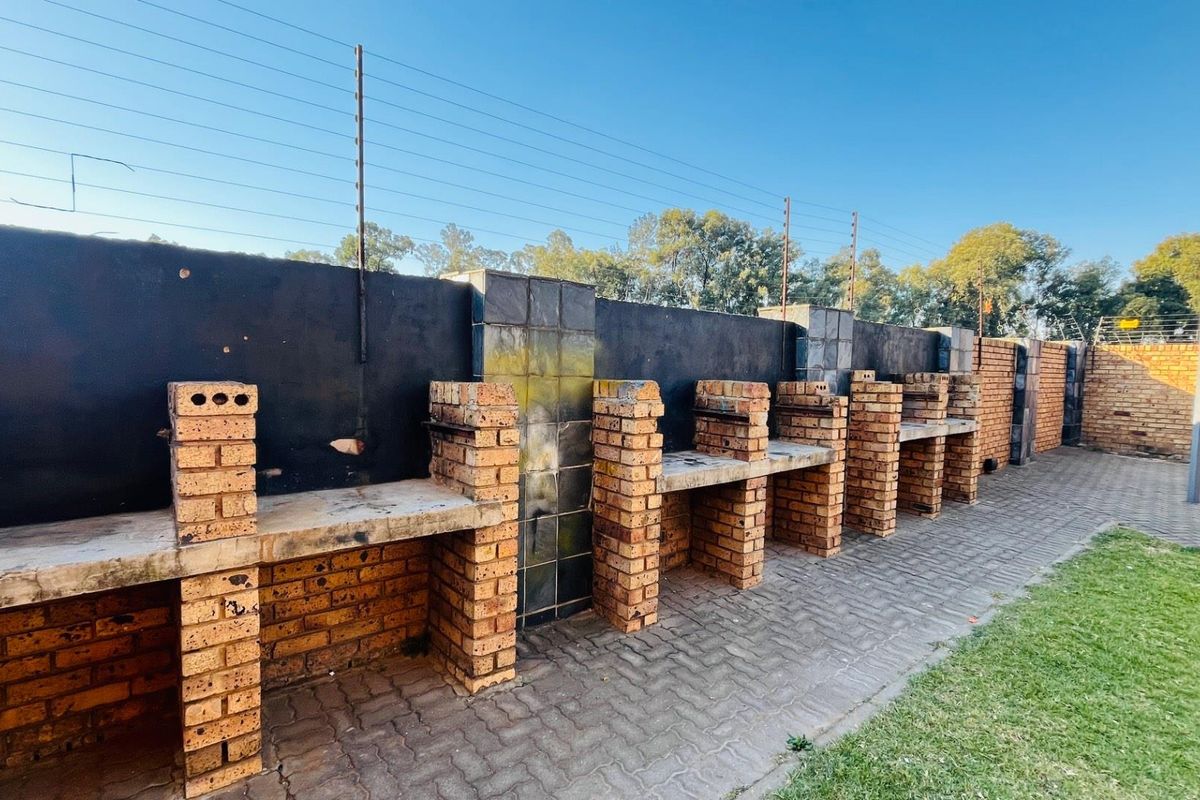 Outdoor communal area featuring multiple built-in brick braai stations with concrete countertops, set against a perimeter wall with electric fencing.