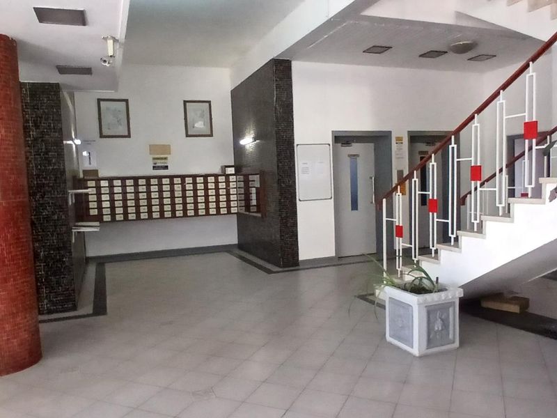 A spacious apartment building lobby featuring a staircase, elevator access, and a wall of mailboxes with tiled flooring.