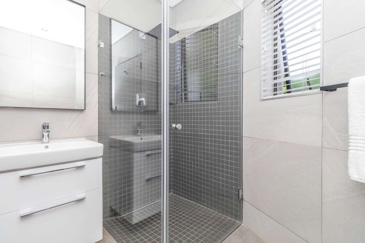 Modern bathroom featuring a glass-enclosed shower with grey mosaic tiling, a contemporary vanity unit, and a wall-mounted mirror.