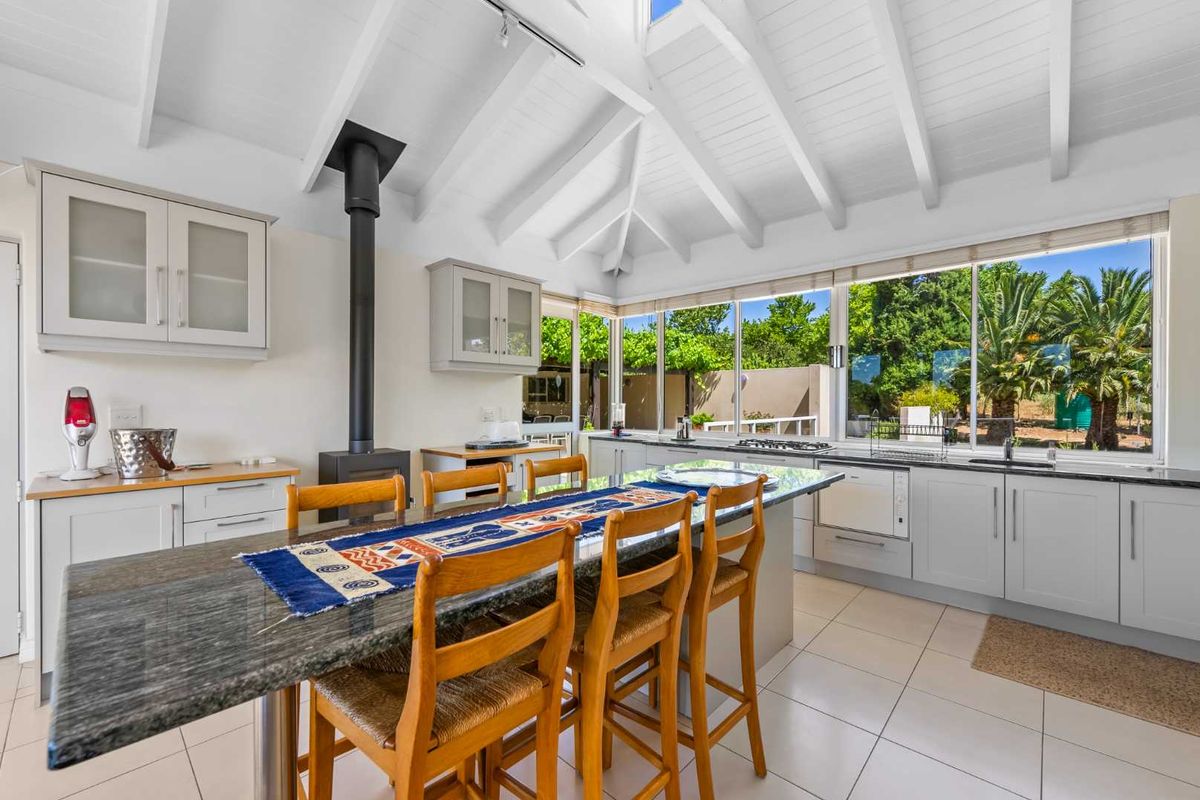 Bright, modern kitchen featuring a vaulted ceiling with exposed beams, granite countertops, a central island, and a freestanding fireplace, overlooking the garden.