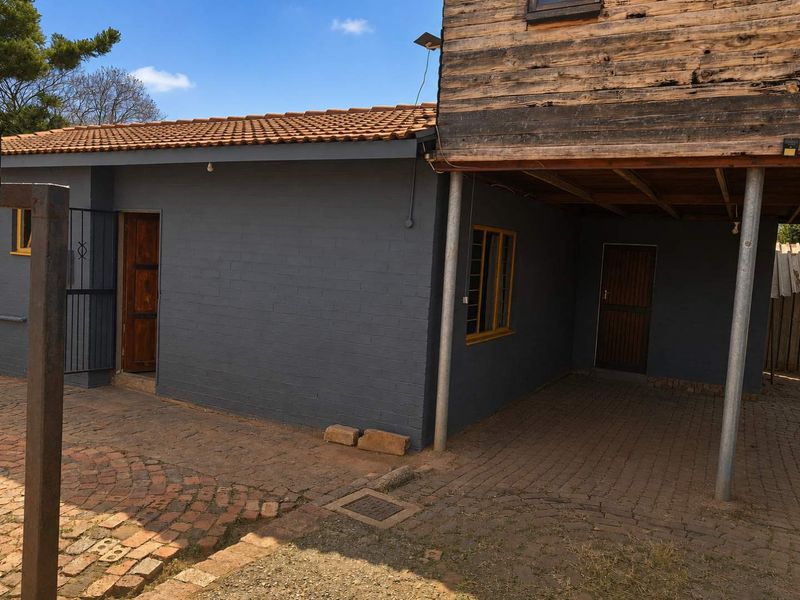 Rear exterior view of the property featuring a paved courtyard area, brick walls, and a raised timber-clad structure supported by steel columns.